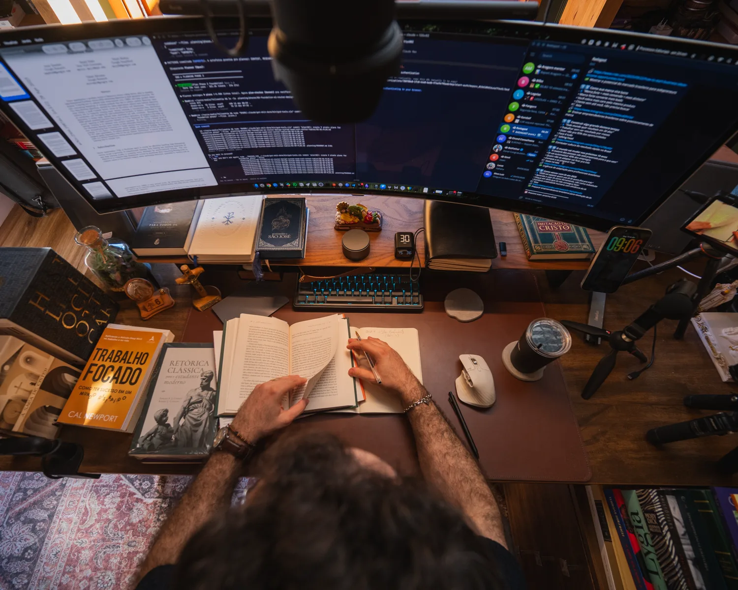 Mesa de estudo do Elton vista de cima, com livros e telas de trabalho